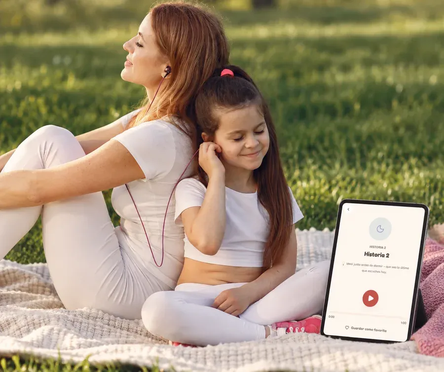 Una mamá y su hija descansando en el pasto, escuchando juntas una historia desde la app